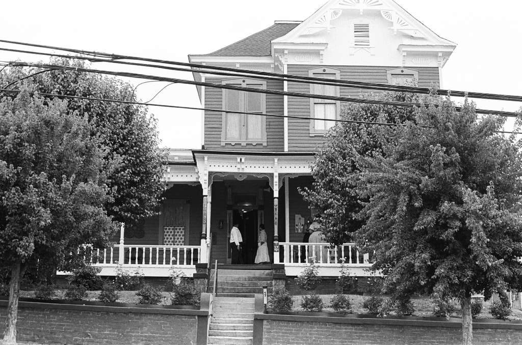 A two-storey Victorian house with a wide porch, behind trees, in Montgomery.